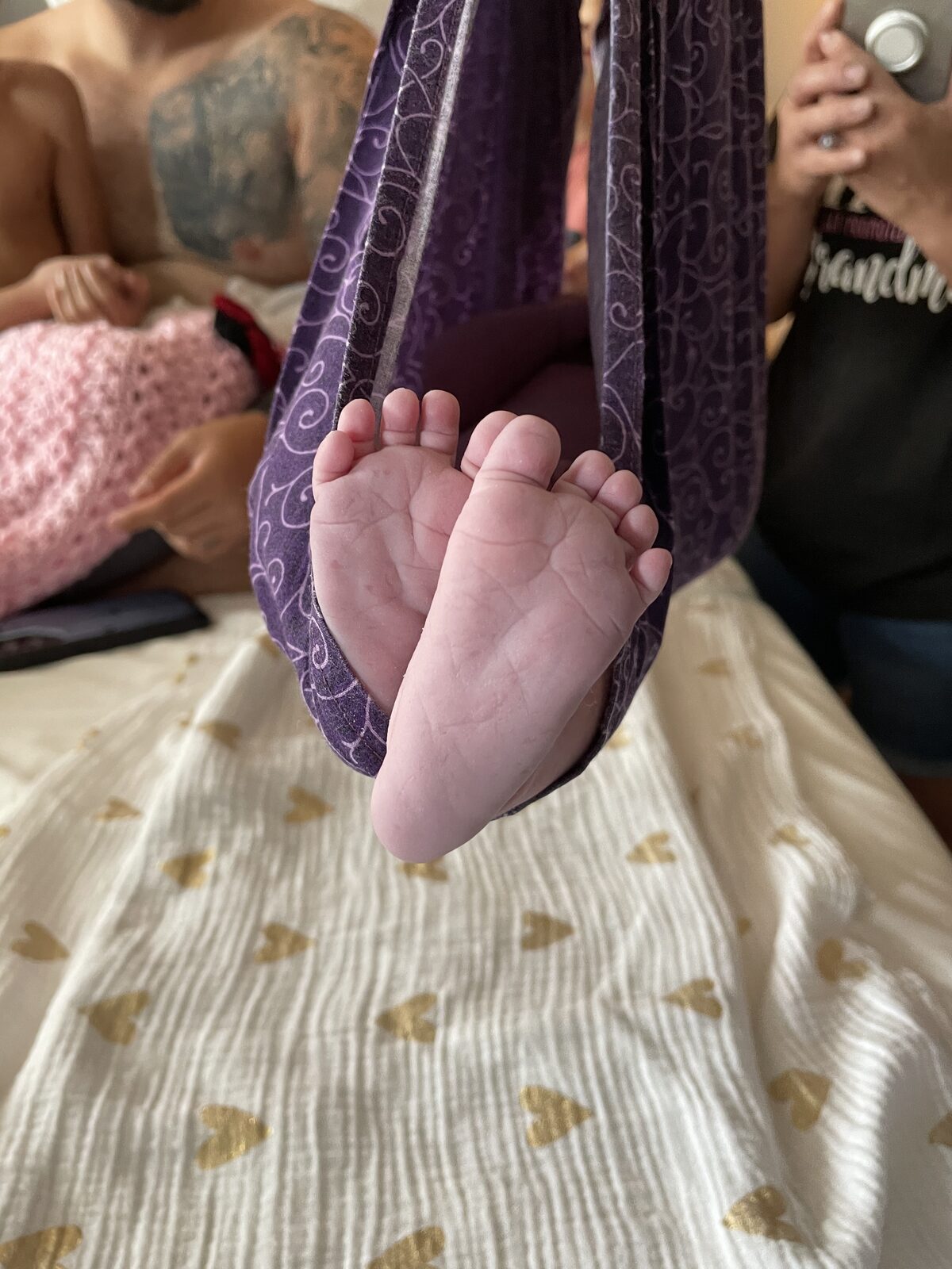 Newborn feet resting in a purple sling